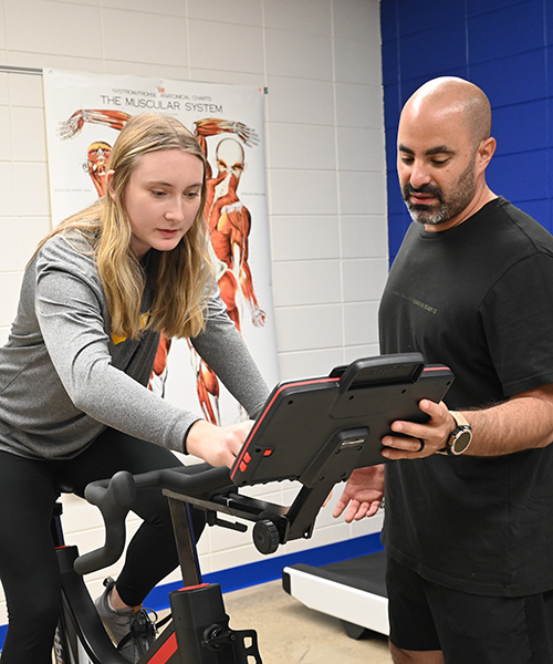 Female student on stationary bike with instructor. 